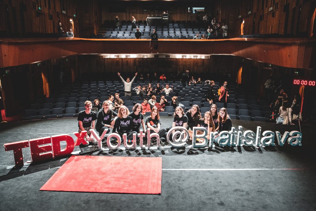 Organizačný tím TEDxYouth @Bratislava v kinosále s veľkým nápisom podujatia.