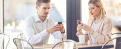Žena s mužom spolu sedia za stolom v kaviarni, obaja pozerajú do svojich mobilných telefónov.