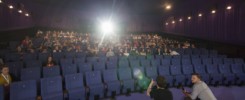Fotografia z Festivalu slovenského filmu v Partizánskom. Desiatky ľudí sedia v kinosále, na okraji pódia sedia dvaja muži a prihovárajú sa publiku.